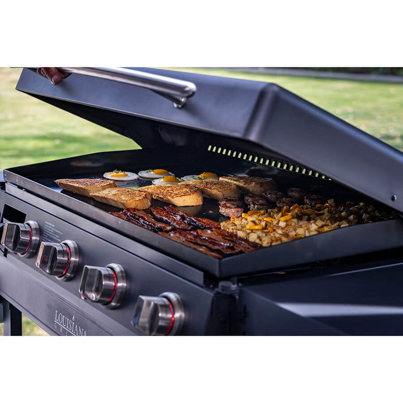 Louisiana Grills 4-Burner Gas Griddle with Ceramic Top. opening lid to reveal food being cooked
